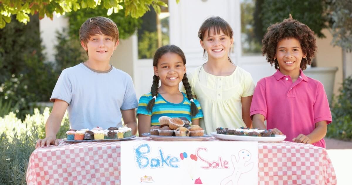 The photo shows children organising a fundraising bake sale event at their school.