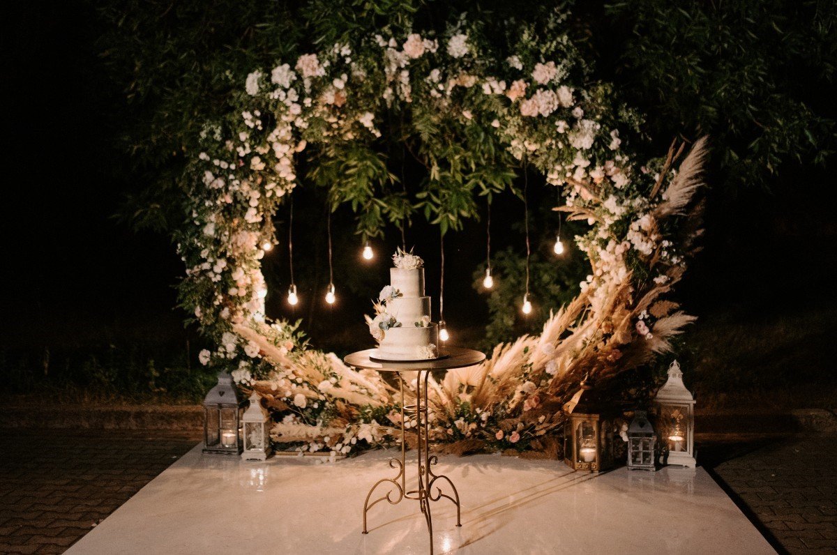 A photo of a wedding backdrop with a wedding cake and a circle made of flowers and green leaves