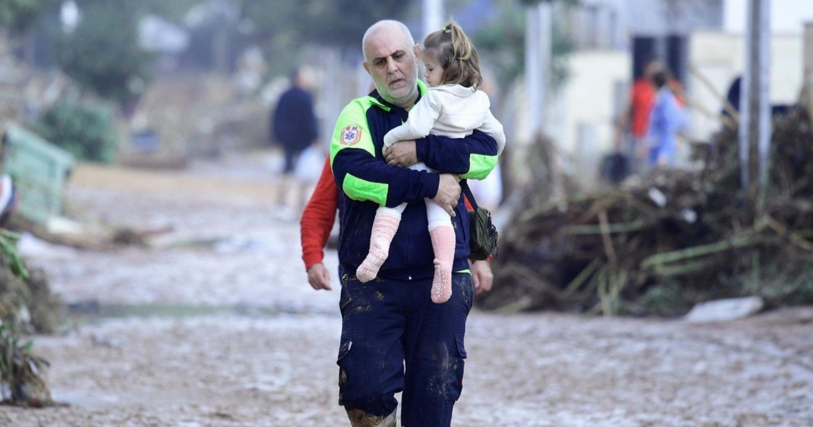 A lifeguard is carrying a little girl in his arms. In the background you can see the landscape after the passage of the flood wave