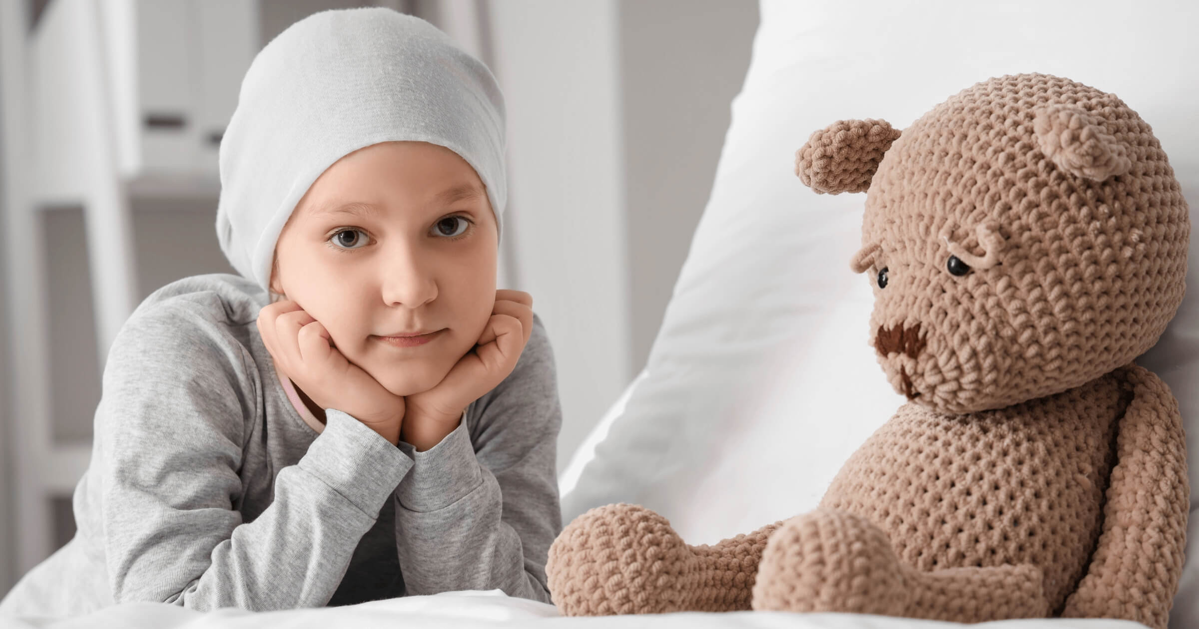 The picture shows a child with cancer sitting next to a teddy bear.