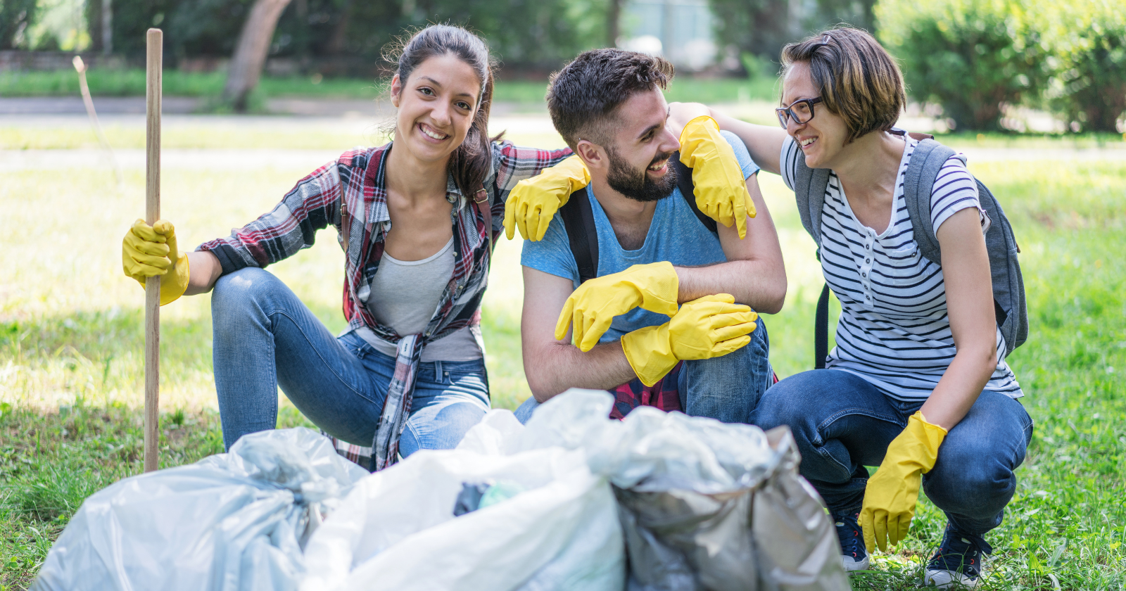 Photo shows two smiling young women and a man taking care of the environment.