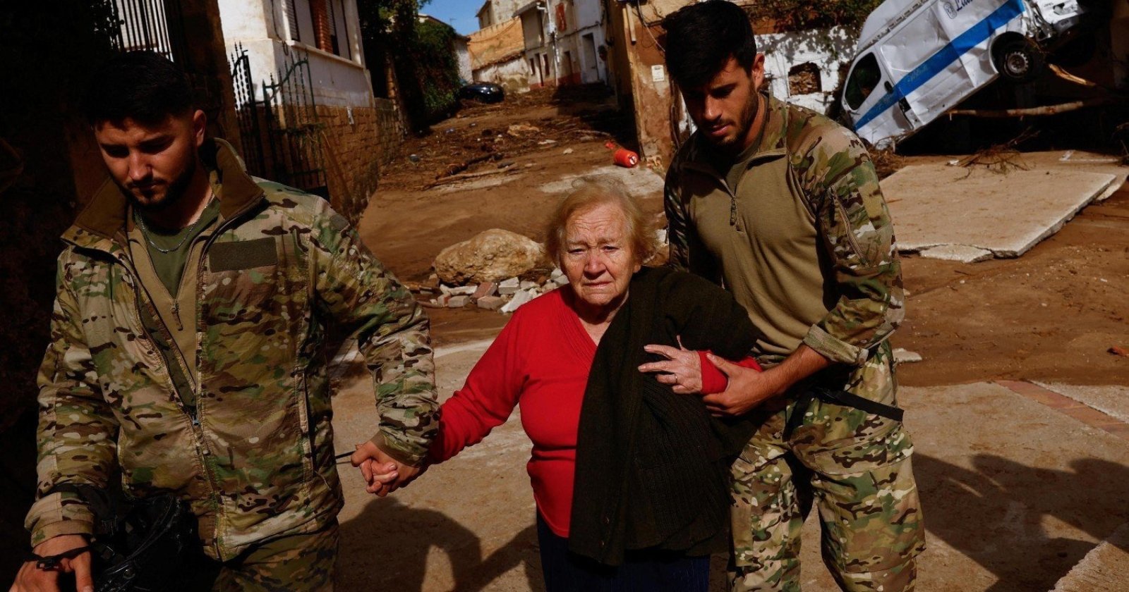 Two young soldiers lead an elderly lady out of her flood-damaged home. The old lady is horrified by the effects of the disaster. She is probably in shock