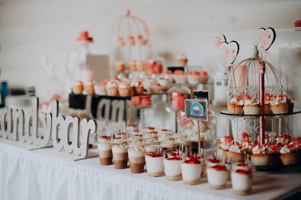 The photo shows a table of sweet snacks. One of the plates next to the sweet monoporations bears the logo of the patisserie